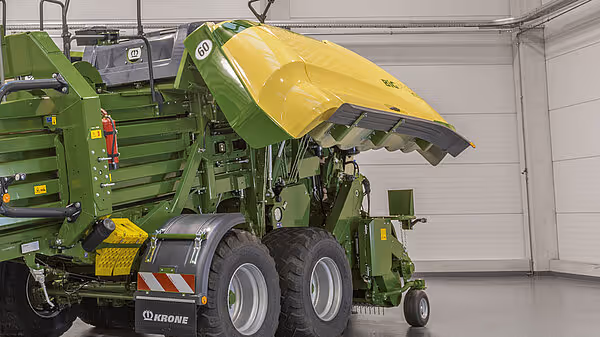 KRONE Big Pack Gen 5 storballpresse med åpen lokk i grønn og gul farge, stående i et lagerbygg. Maskinen har doble hjul og hydraulisk løftearmer.