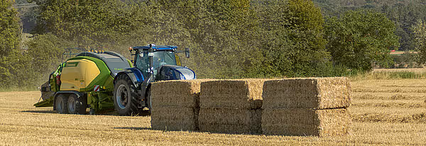 KRONE Big Pack storballpresse på stubbeåker med ferdigpressede store firkantede baller stablet bak maskinen. Blå traktor trekker den grønne og gule pressen.