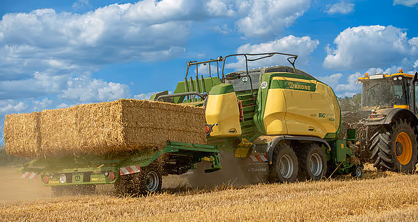 KRONE Big Pack storballpresse i drift på kornåker med store firkantede baller i bakgrunnen. Maskinen har gul og grønn fargekombinasjon.