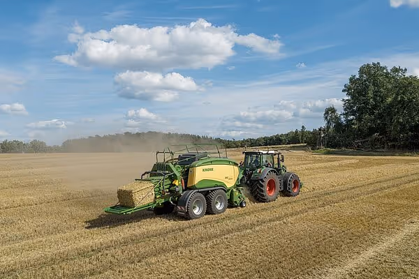 KRONE Big Pack HDP II storballpresse i arbeid på åker, trukket av rød traktor under blå himmel.