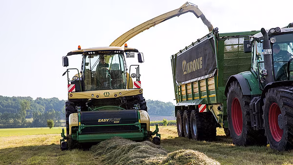 Krone Big X som høster gras og fyller tilhenger under arbeid på jordet.