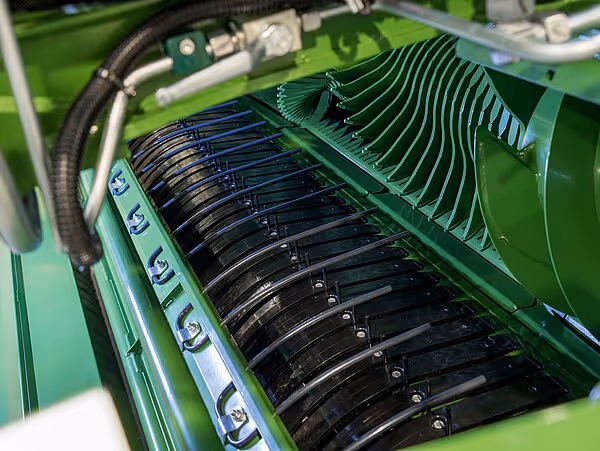 Nærbilde av oppsamlingskammeret i en KRONE CombiPack med sorte tannhjul og grønne metallplater som leder høyet oppover.