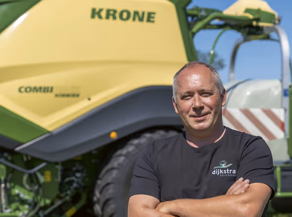 En mann med kryssede armer står foran en KRONE CombiPack HDP rundballpresse, iført mørk t-skjorte med Dijkstra-logo.