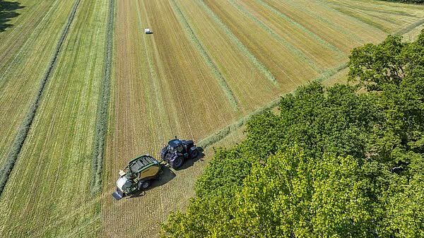 Luftfoto av en traktor med KRONE CombiPack HDP som arbeider på en åker med striper av grønt og brunt gras.
