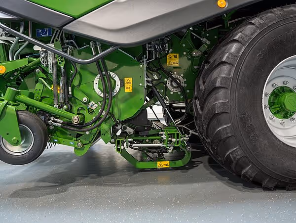 Detaljbilde av hydrauliske komponenter og mekaniske deler på en grønn KRONE CombiPack HDP maskin. Gule advarselsmerker er synlige på utstyret.