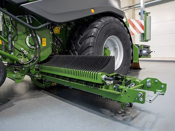 Nærbilde av Krone CombiPack HDP landbruksmaskin som viser den grønne undertillen med pakkervalse og store hjul inne i et lagerbygg.