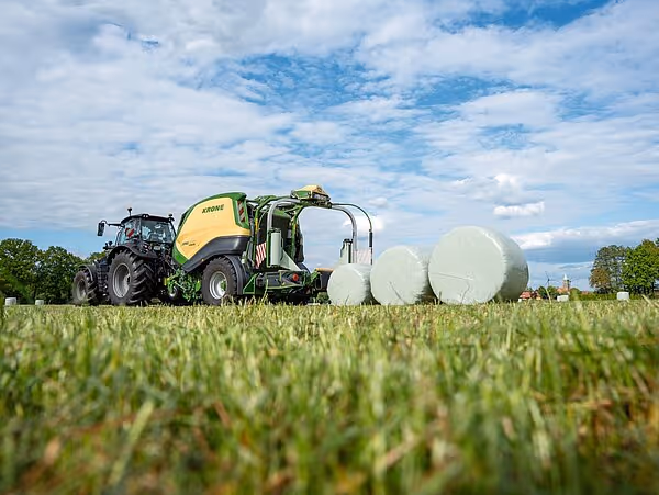 KRONE Combipack-HDP rundballpresse trukket av traktor på eng, med ferdige hvite plastballer i bakgrunnen.