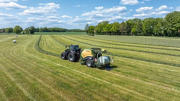 Luftfoto av traktor med KRONE Combipack-HDP som presser rundball på slått eng med stripemønster.