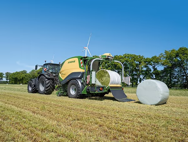 KRONE Combipack-HDP i arbeid på slått mark med nylagd hvit plastball og vindmøller i bakgrunnen.
