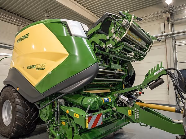 En KRONE CombiPack ballepresse med grønn og gul fargekombinasjon står parkert inne i et verksted.