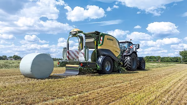 KRONE CombiPack HDP rundballpresse i arbeid på slått åker med ferdig plastinnpakket rundball ved siden av.