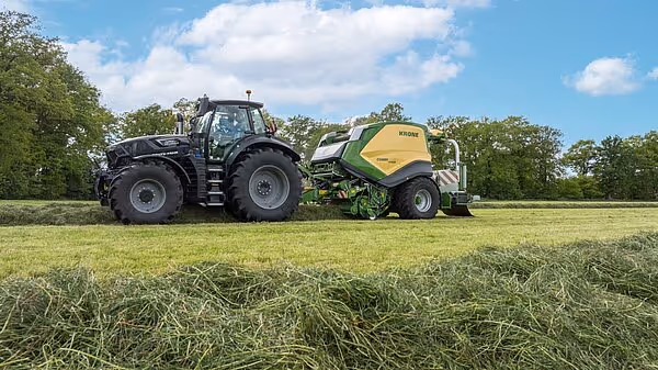 Traktor med tilkoblet KRONE CombiPack HDP ballepresse arbeider på slått eng.