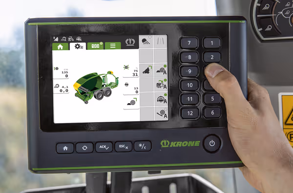 Hånd som betjener digitalt kontrollpanel med trykkknapper og skjerm inne i traktorkabinen.