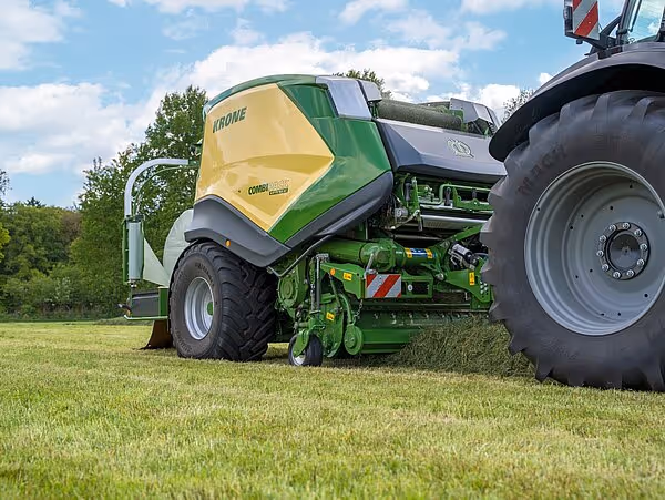 KRONE CombiPack HDP ballepress i arbeid på gressmark, trukket av traktor på en solskinnsdag.