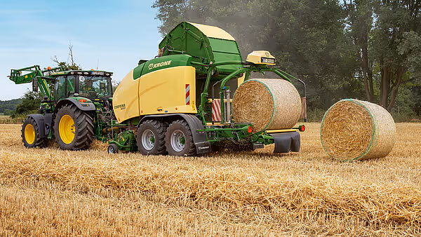 KRONE Comprima Plus rundballpresse i arbeid på stubbåker med ferdigproduserte rundballer. Maskinen trekkes av grønn traktor og produserer store halmballer.