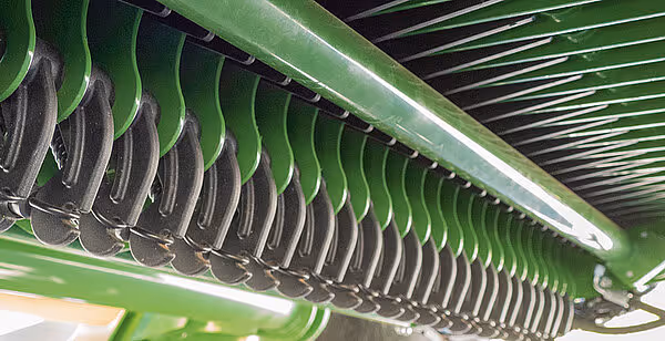 Nærbilde av Krone Comprima Plus sin pick-up-enhet med grønne spiralfjærer og tagger for oppsamling av høy.