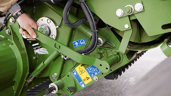 Detaljbilde av hydrauliske koblinger og smørepunkt på Krone Comprima Plus, med hånd som demonstrerer tilgang.