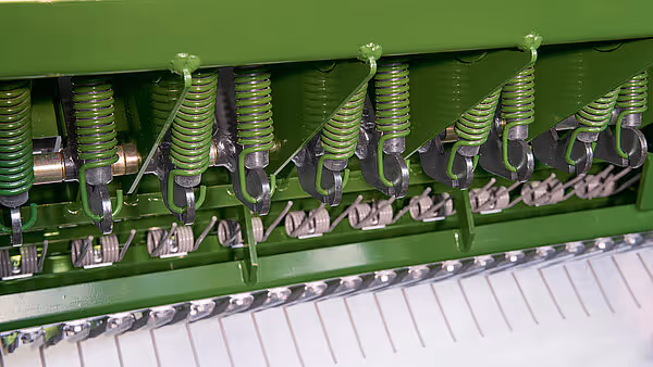 Rekke med grønne spiralfjærer og klamrer på balepressen som sikrer jevn høystrøm inn i balingskammeret.