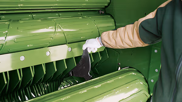 Hånd som åpner serviceluken på Krone Comprima Plus for tilgang til indre komponenter og vedlikehold.