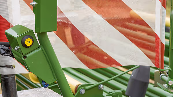 Nærbilde av grønn KRONE Comprima Plus rundballpresse som pakker høy eller gress i plastfilm. Maskinen har røde og hvite refleksstrimler for sikkerhet.