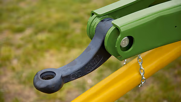 Nærbilde av grønt trekkoppling på gul landbruksmaskin, med kjetting og metallbeslag.