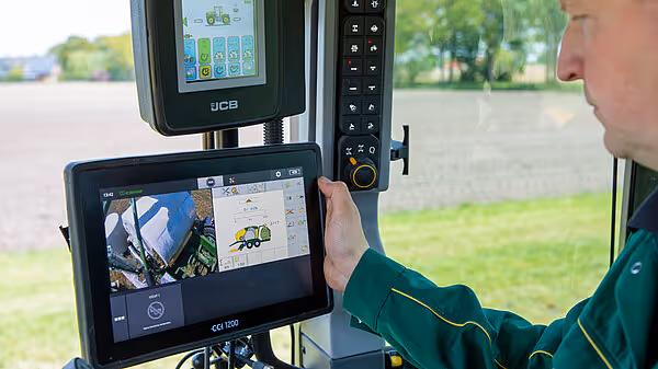 Traktoroperatør bruker ISOBUS-terminal i førerhus, med kameraskjerm og kontrollpanel synlig.