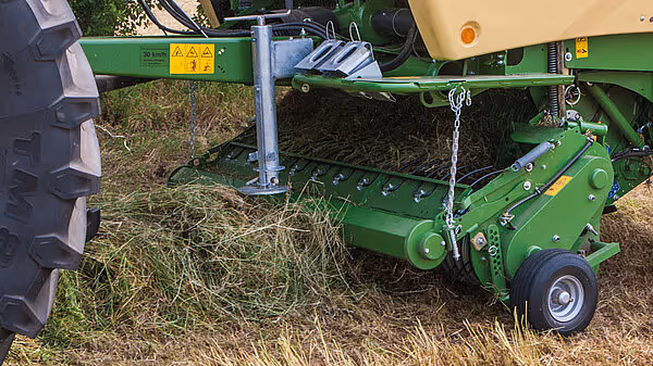 KRONE Comprima rundballpresse samler opp høy med oppsamlingsmekanismen synlig.