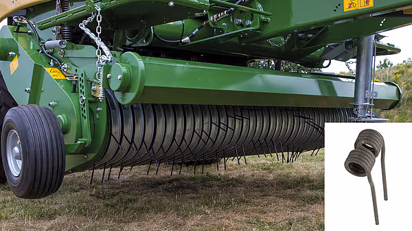 Underside av KRONE Comprima som viser oppsamlingsvalsen med sorte gummitiner. En reservetine er vist separat til høyre i bildet.