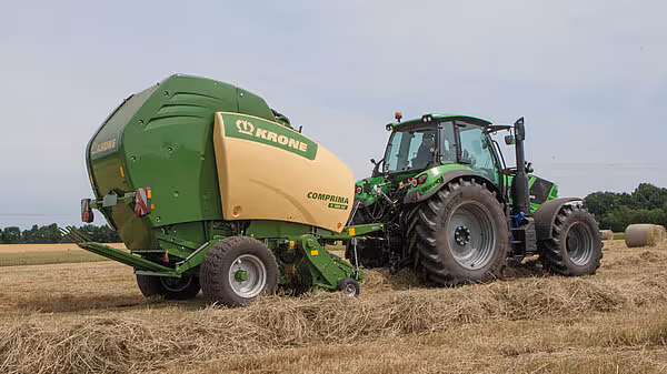 KRONE Comprima rundballpresse trukket av Deutz-Fahr traktor på stubbeåker med spredte rundballene i bakgrunnen.