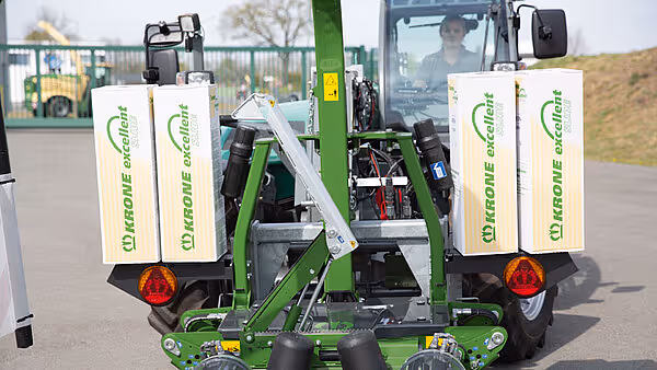 Bakside av KRONE EasyWrap 150 ballpresse med monterte hvite plastfolieruller og røde reflekser, traktor synlig i bakgrunnen.