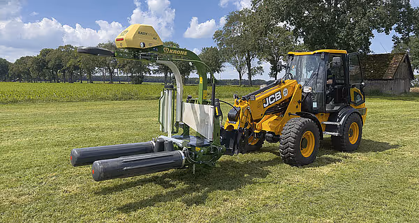 KRONE EasyWrap 150 rundballepresse tilkoblet gul JCB traktor på grønn mark med uthengde plastballer.