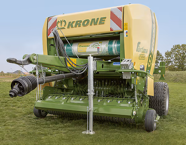KRONE Fortima rundballpresse i grønt og gult står på eng med support-ben nede. Maskinen har store hjul og er klar for bruk.