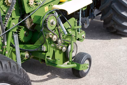 Nærbilde av drivsystemet på en grønn KRONE Fortima rundballpresse, som viser tannhjul, kjeder og kraftoverføring.