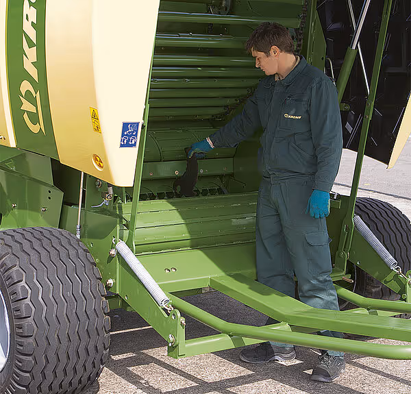 Tekniker i arbeidsklær utfører vedlikehold på KRONE Fortima rundballpresse.