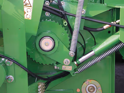 Detaljbilde av Krone Fortima sitt indre drivverk med tannhjul og spiralfjær. Hydraulikkslanger og mekaniske komponenter er montert på grønn maskinramme.