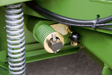 Gul hydraulisk komponent med spiralform montert på grønn maskinramme. Hydraulikkslanger og spiralfjær er koblet til komponenten.