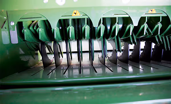 Knivsystem i Krone Fortima rundballpresse med flere sorte kniver montert i grønn ramme. Knivene er plassert i rekke for kutting av høy eller halm.