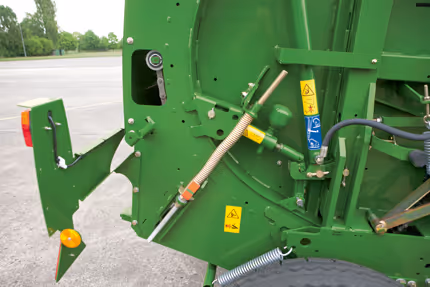 Detaljbilde av hydrauliske komponenter og sikkerhetsetiketter på Krone Fortima rundballpresse. Hydraulikkslanger og betjeningsenheter er synlige.