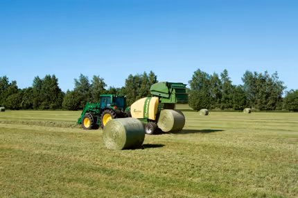 KRONE Fortima rundballpresse i arbeid på en åker med ferdig rundball. Pressen er trukket av en grønn traktor og produserer store rundball.