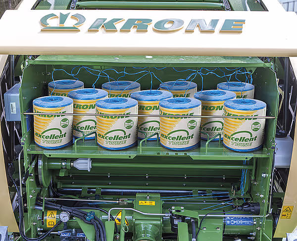 Krone Fortima rundballpresse med åpen lokk som viser lagring av Excellent pressgarn i blå og gule beholdere.