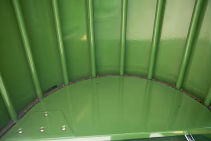 Innvendig bilde av presskammeret i Krone Fortima rundballpresse med grønne vegger og buet form. Metallbolter for festing av belter eller ruller er synlige.