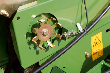 Nærbilde av rotorblad eller kuttemekanisme på KRONE Fortima rundballpresse. Gul advarselsetikett er festet på den grønne maskindelen.