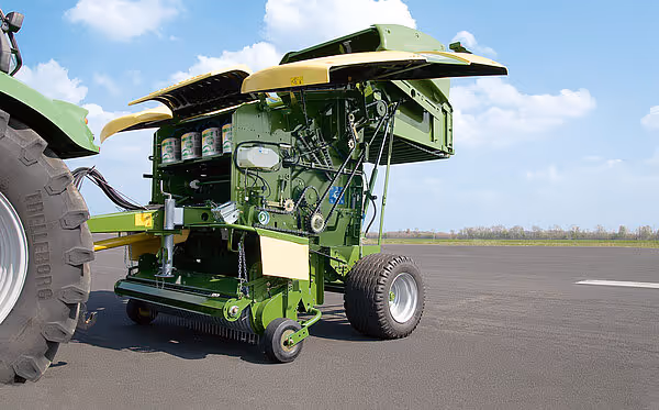 KRONE Fortima rundballpresse i arbeidsposisjon på asfalt med åpen bakluke. Maskinen er koblet til traktor og klar for bruk.