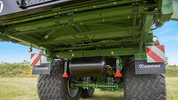 Underside av KRONE MX silohakker med hydraulisk sylinder og doble store landbruksdekk med rødt og hvitt varselmerke.