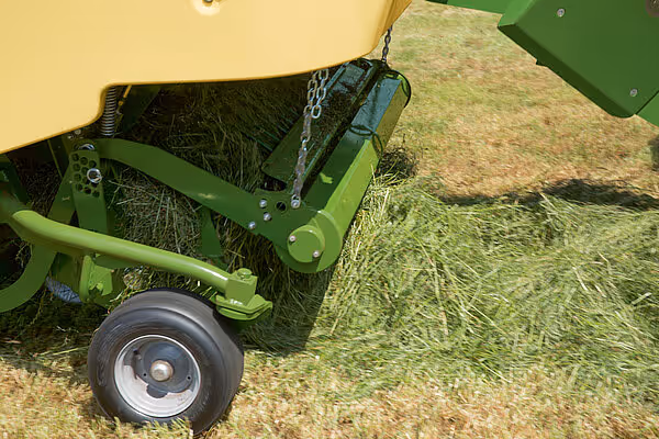 Sidevisning av en grønn KRONE MX høstmaskin med rotorbørste lastet med høy, hjul og kjetting synlig.