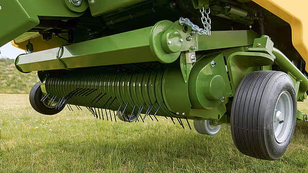 Undersidevisning av KRONE MX høstmaskin som viser rotorbørste med sorte tenger, drivaksel og hjul på grønt underlag.