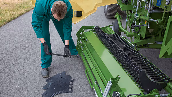 Servicetekniker løfter og viser en utslitt sortplastdel fra KRONE MX såmaskinen.