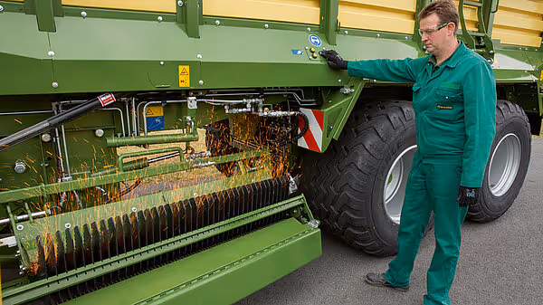 Serviceteknikker inspiserer rotorkammen på en KRONE MX fôrutspreader med synlig jordforurensning på arbeidsdelen.