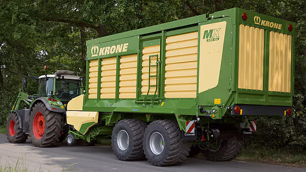 KRONE MX silofôrvogn med full last transportert av grønn traktor på asfaltert vei.