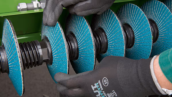 Nærbilde av turkoise slipeskiver montert på rotorakselen med svart arbeidshanske som demonstrerer størrelsen.